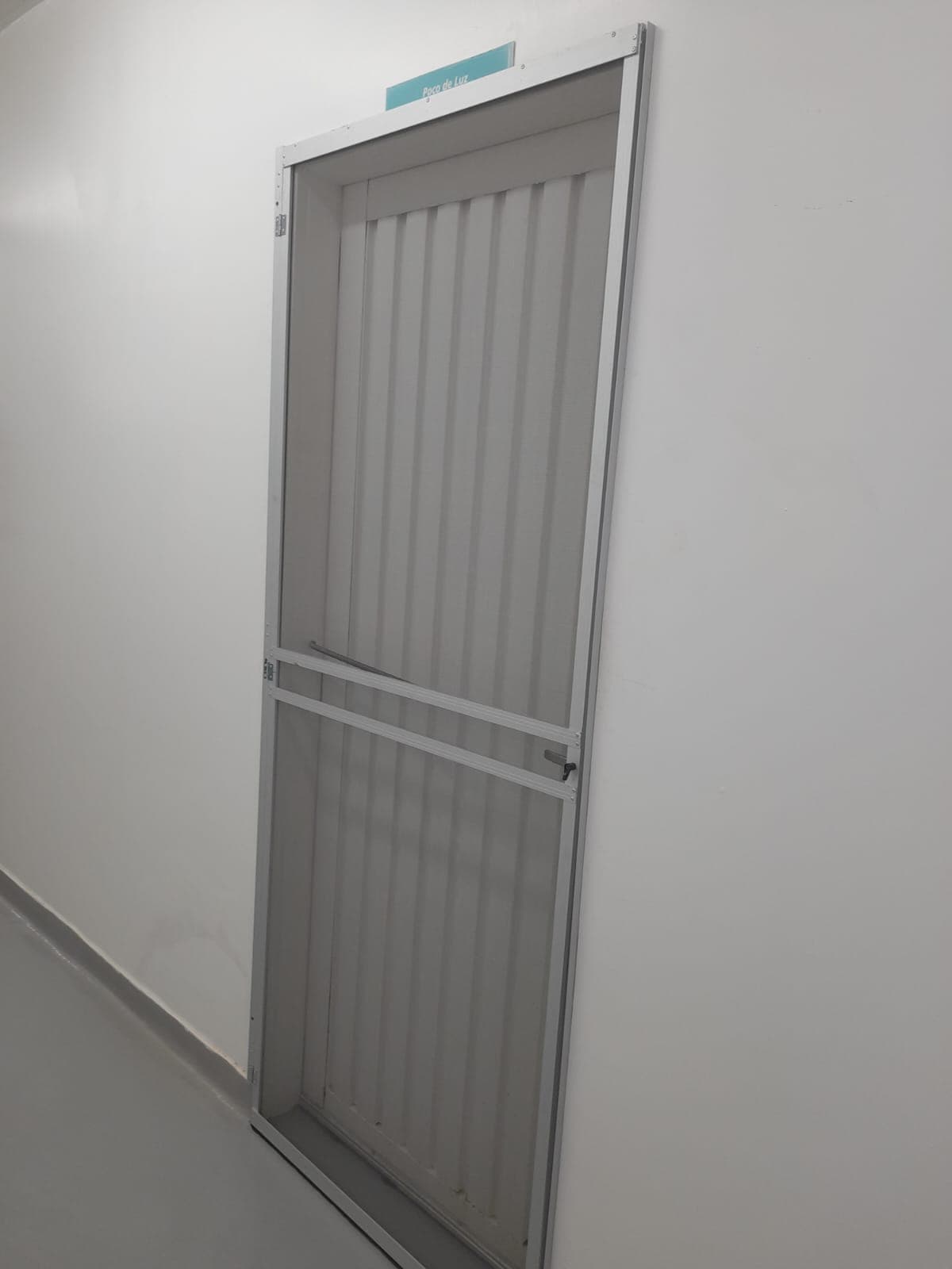 Porta de tela mosquiteira com perfil de alumínio branco instalada em passagem interna de ambiente comercial