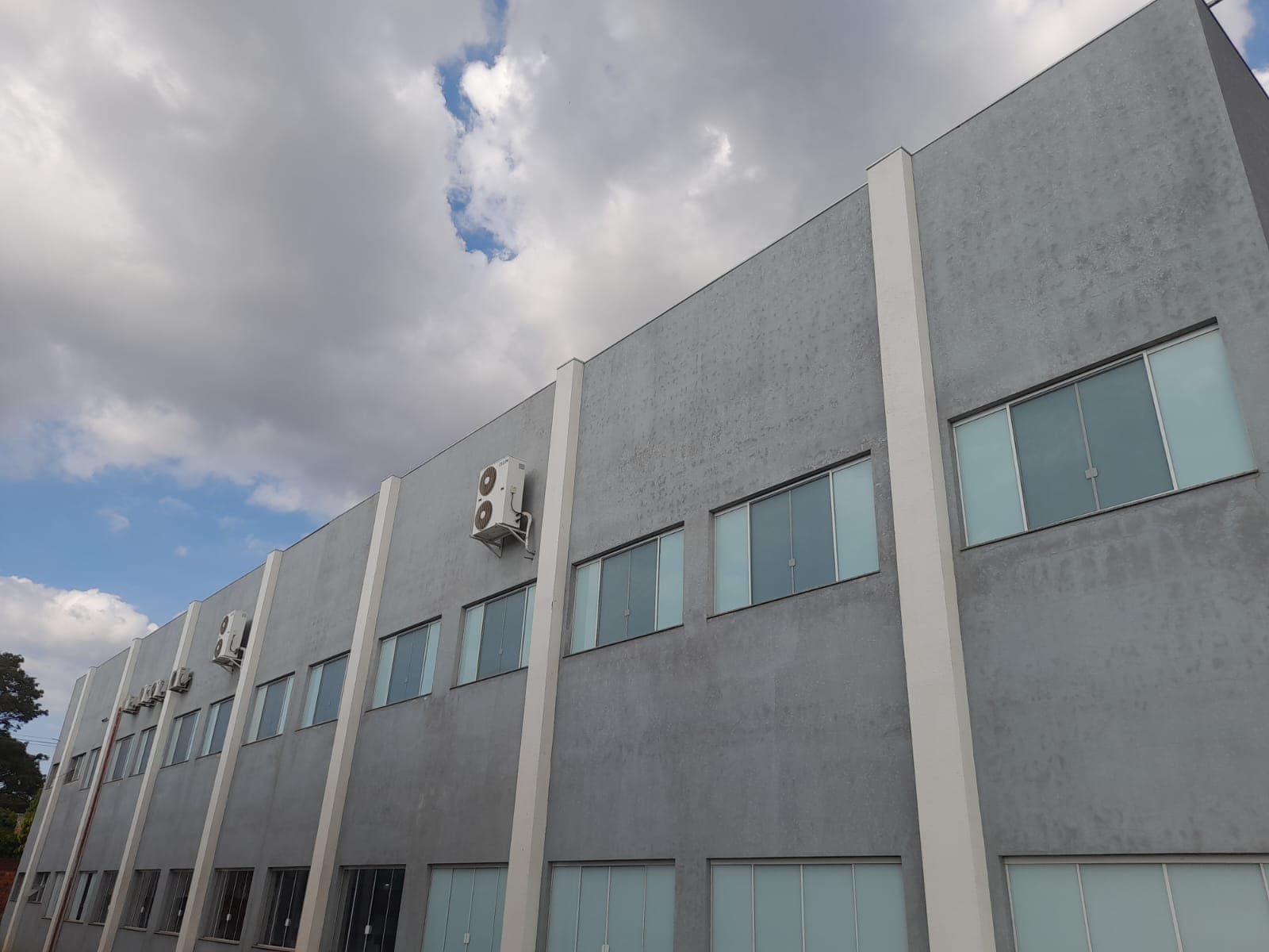 Fachada de prédio industrial de dois andares com faixa de janelas onde foram instaladas telas mosquiteiras