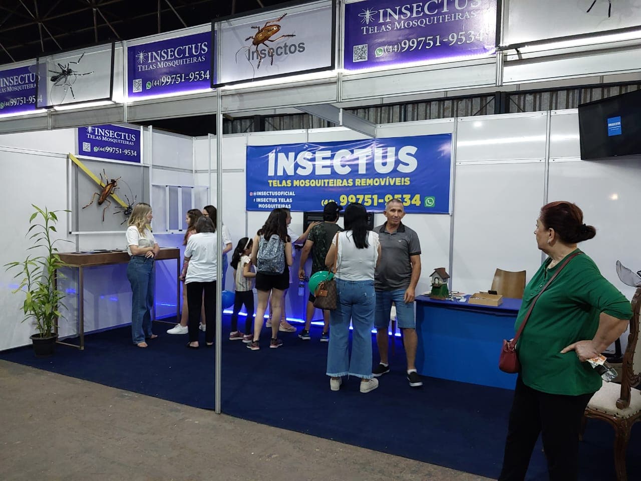 Estande da Insectus em feira do setor, com visitantes no balcão e painéis de telas mosquiteiras removíveis