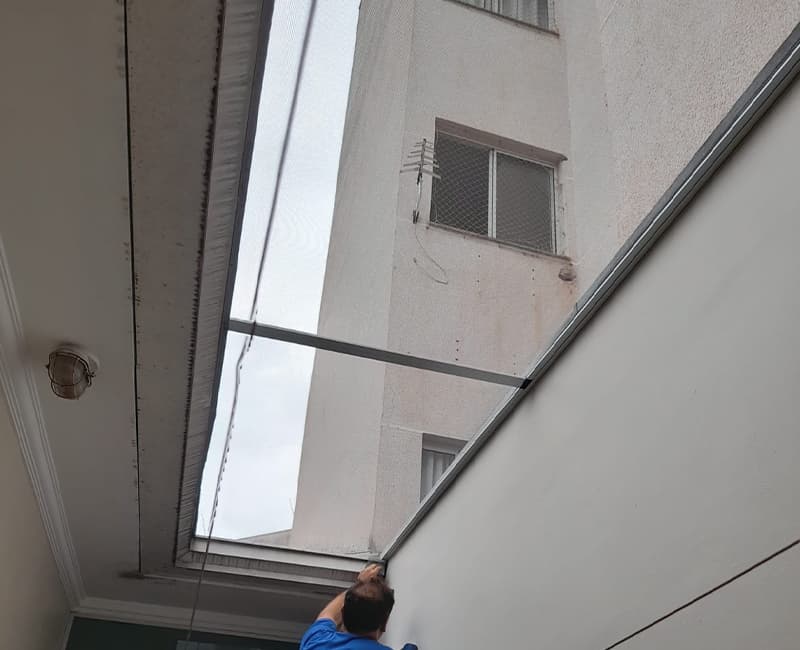 Instalador da Insectus fixando tela mosquiteira em trilho de alumínio no topo de um poço de luz entre prédios
